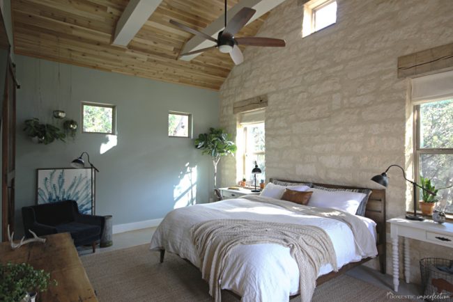 rustic farmhouse master bedroom with wood ceiling and stone wall